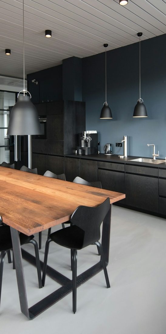 Moderne Küche mit Holz-Esstisch, schwarzen Stühlen und eleganten Pendelleuchten.