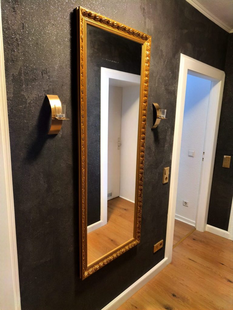 Ein schmaler, goldgerahmter Spiegel an einer schwarzen Baumwoll-Wand im Flur.