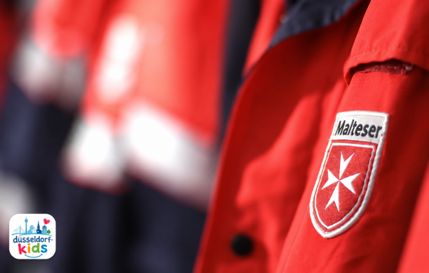 Rote Jacken mit dem Emblem des Malteserordens im Hintergrund.